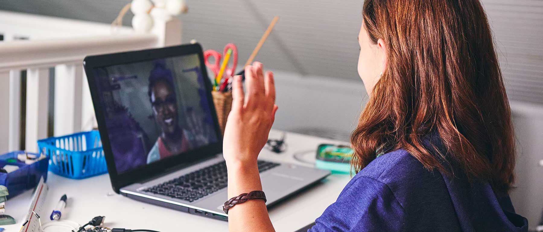 Student raising her hand in front of her laptop image