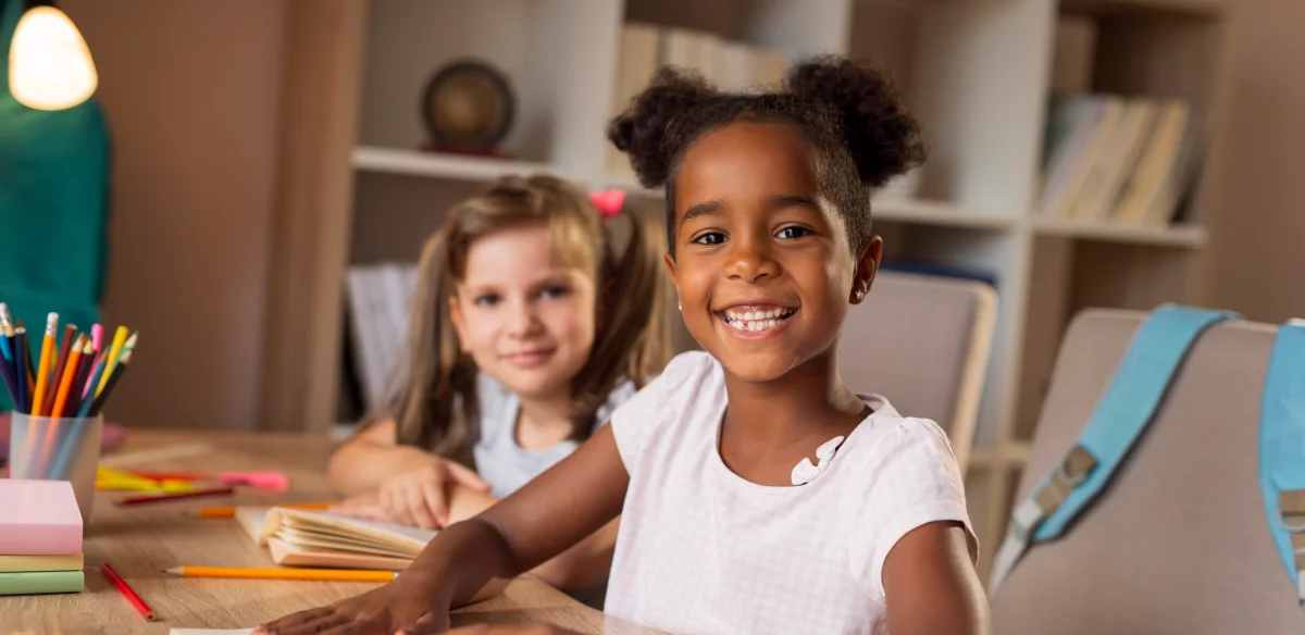 Two students smiling at the camera while doing homework together