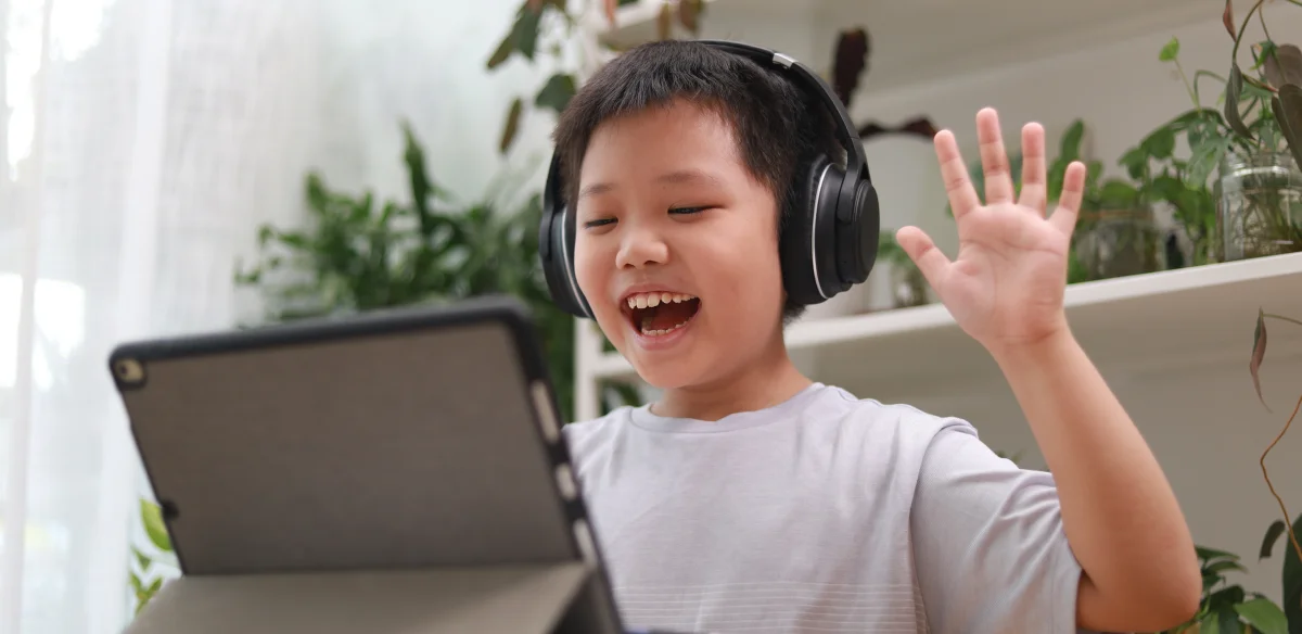 Elementary student wearing a black pair of headphones while attending to an online class with his tablet