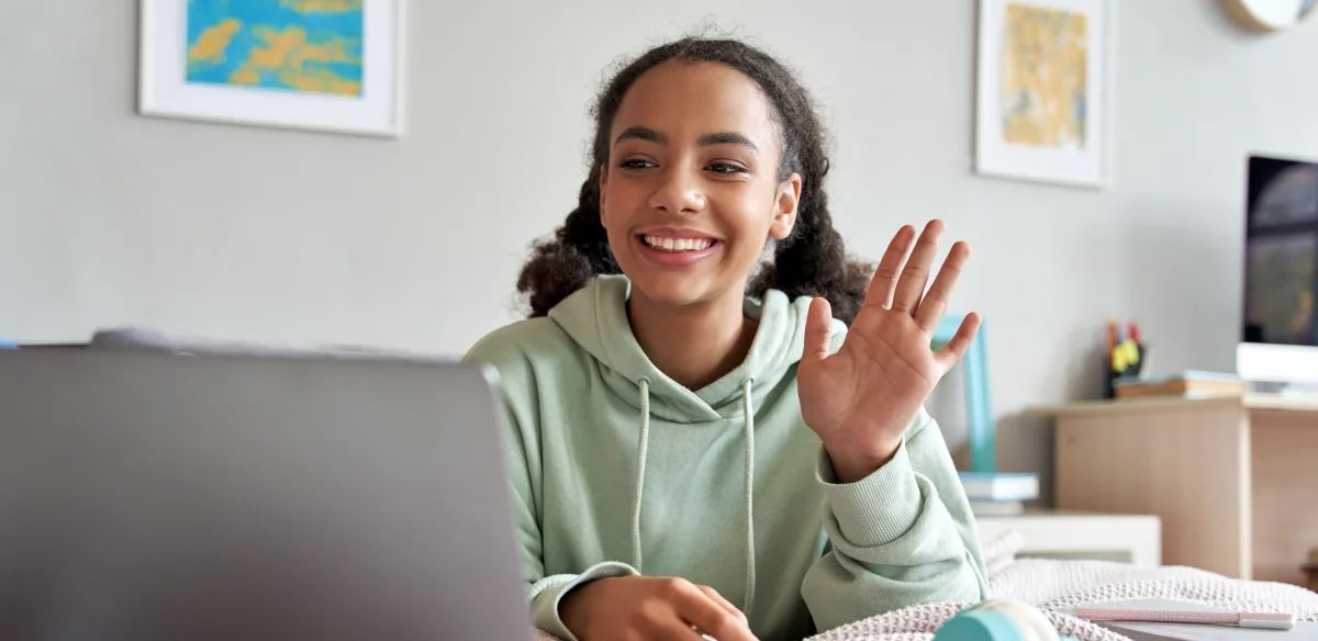 High school student waiving at her online class at home